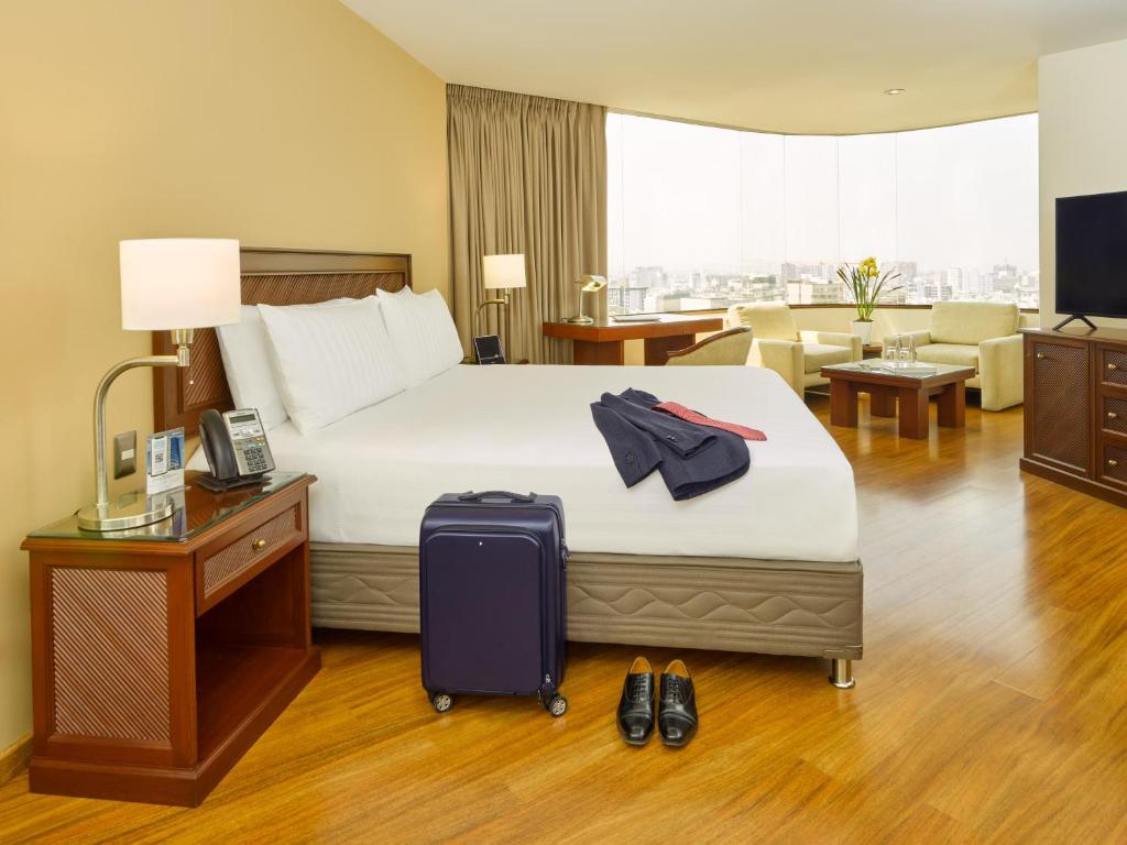 
a hotel room with a bed, desk, chair and luggage at Hotel Estelar Miraflores in Lima
