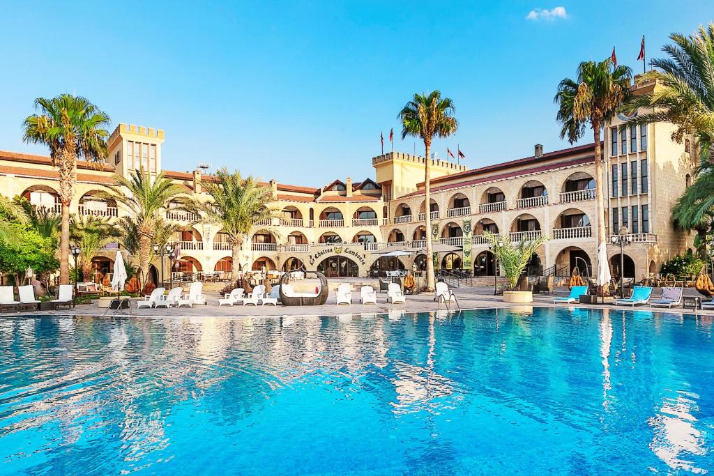 a swimming pool in front of a building with palm trees at Le Chateau Lambousa in Kyrenia
