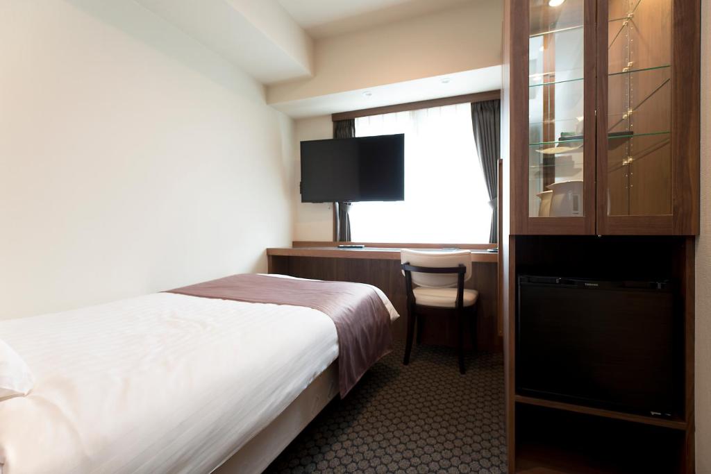 a hotel room with a bed and a desk with a television at Kadoya Hotel in Tokyo