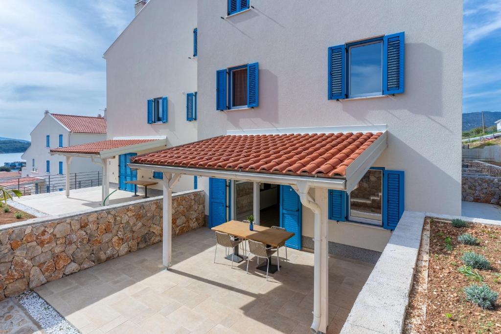 a white house with blue windows and a table at Apartment Blue Monstéra in Cres