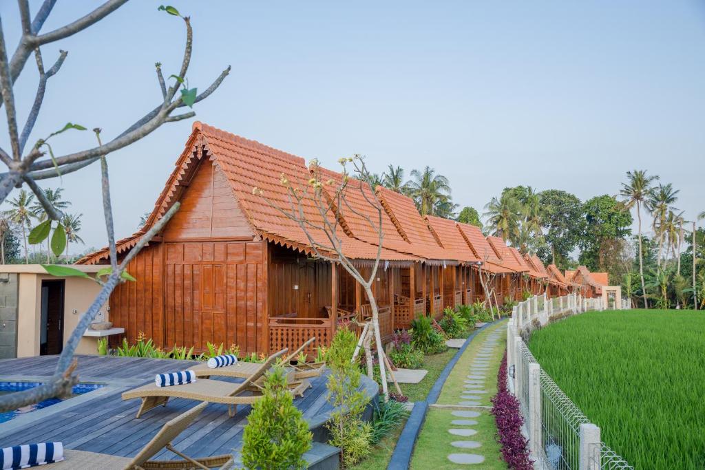 une rangée de bâtiments en bois avec un champ vert dans l'établissement Victory Munggu, à Canggu