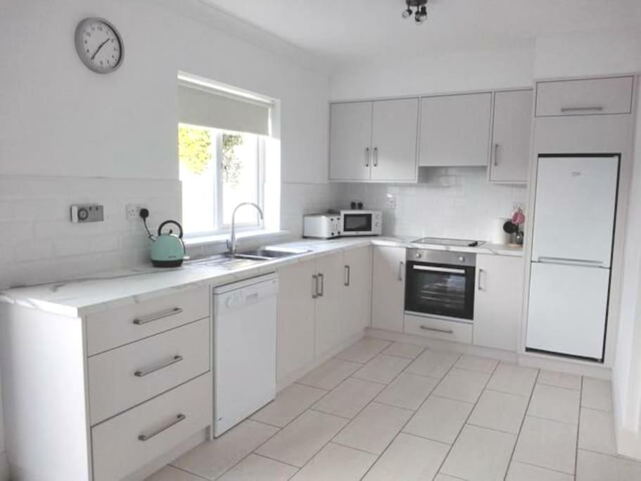a kitchen with white cabinets and a clock on the wall at Townhouse Clifden: Located in the heart of Connemara in Clifden