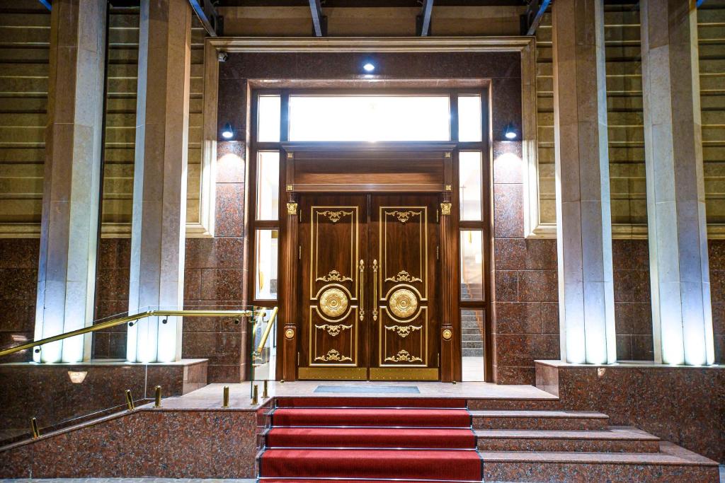 - une grande porte en bois dans un bâtiment doté d'un tapis rouge dans l'établissement Krokus Plaza, à Tachkent