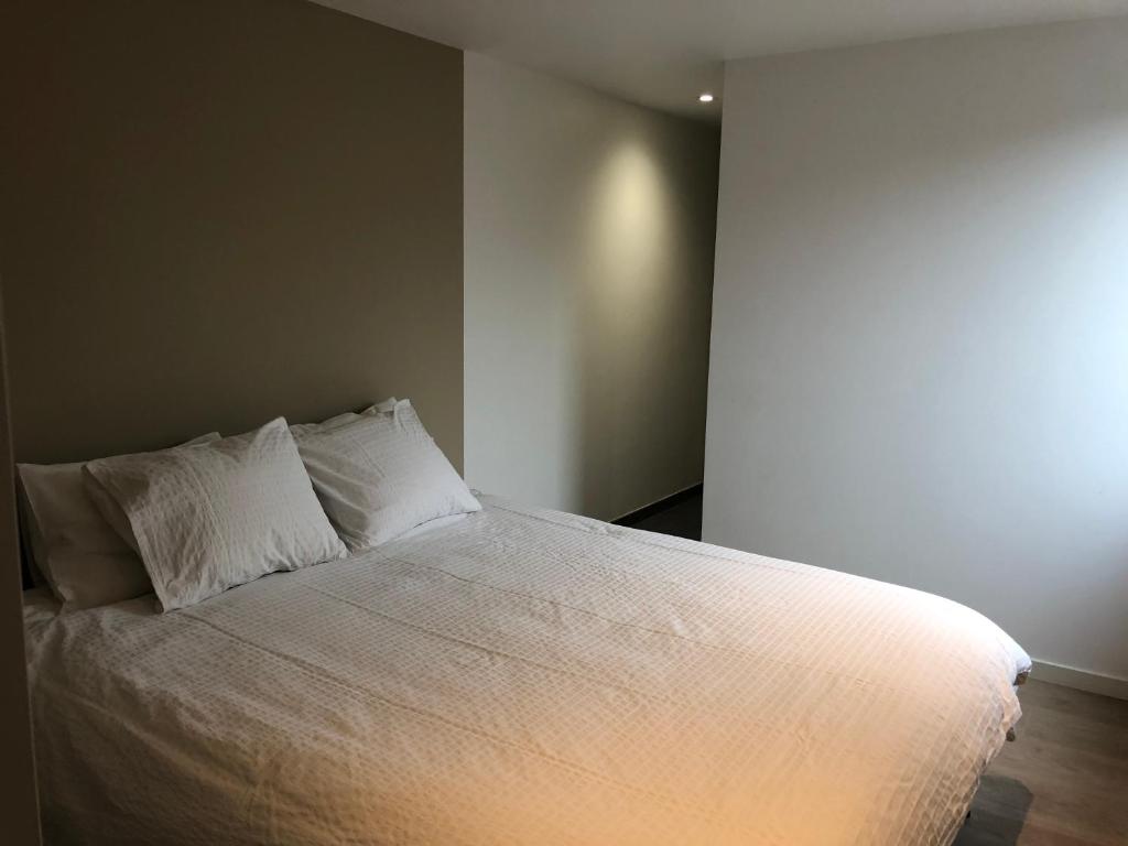 1 cama con sábanas blancas y almohadas en una habitación en La casetta del Nonno, en Floreffe