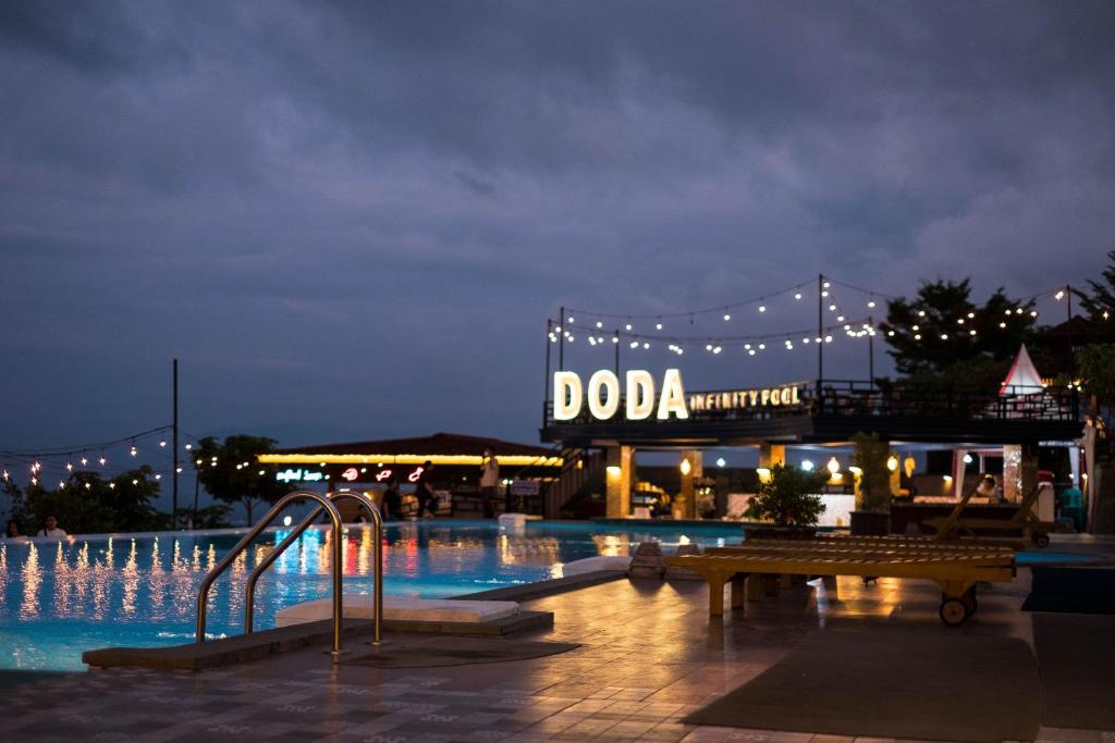 Bukit Indah Doda Hotel & Resorts في بالو: حمام سباحة في الليل مع وجود علامة دودا في الخلفية