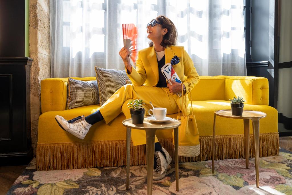 une femme assise sur un canapé tenant une coupe de champagne dans l'établissement Hotel Louis II, à Paris
