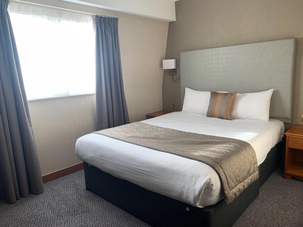 um quarto de hotel com uma cama grande e uma janela em Savera Hotel South Ruislip em Hillingdon