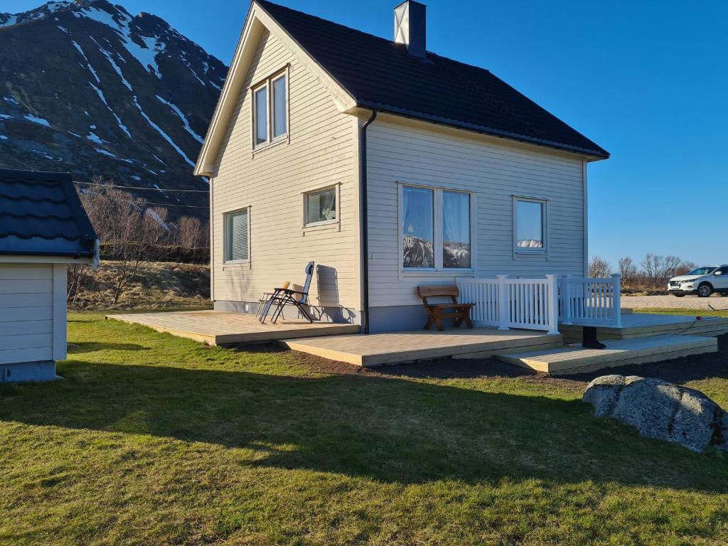 uma pequena casa branca com um deque e uma montanha em Lauvåsstua-Charming house by the sea em Bøstad