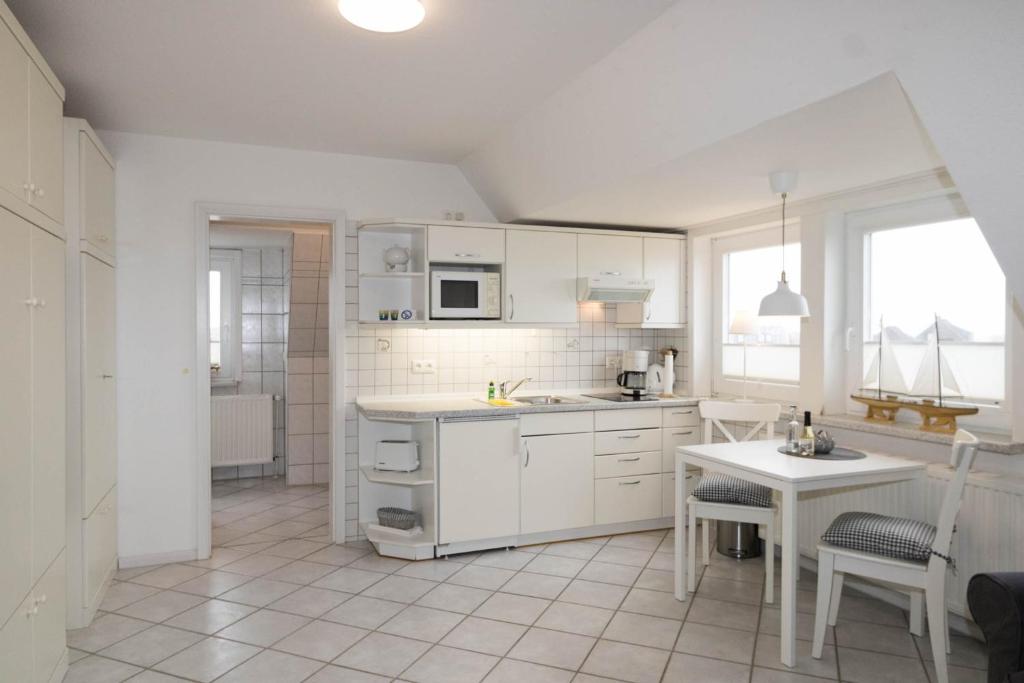 a kitchen with white cabinets and a table with chairs at Hüs Auert Tharep, Wohnung 3 in Hörnum