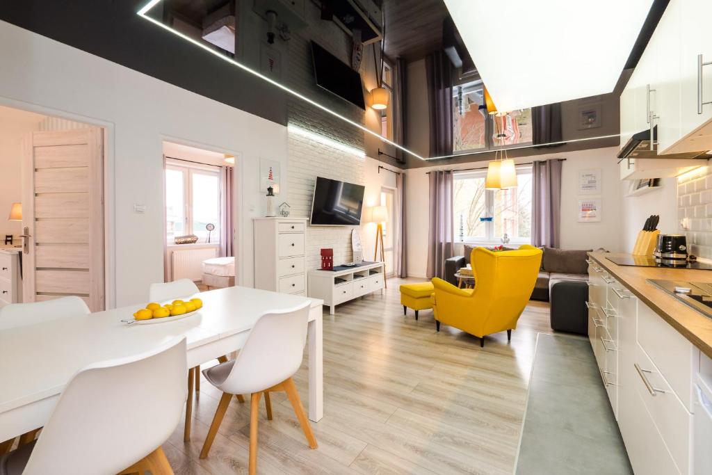 a kitchen and living room with a white table and yellow chairs at Apartamenty Usteckie Wydma in Ustka