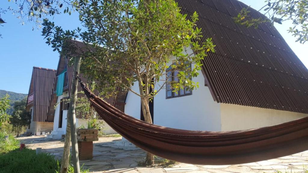 a hammock in front of a building with a tree at Chalé Roots in São Thomé das Letras