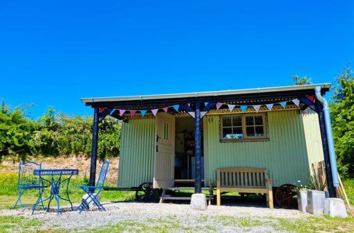 a small green house with a bench and a table at Pen Bryn Shepherd Hut in Hay-on-Wye