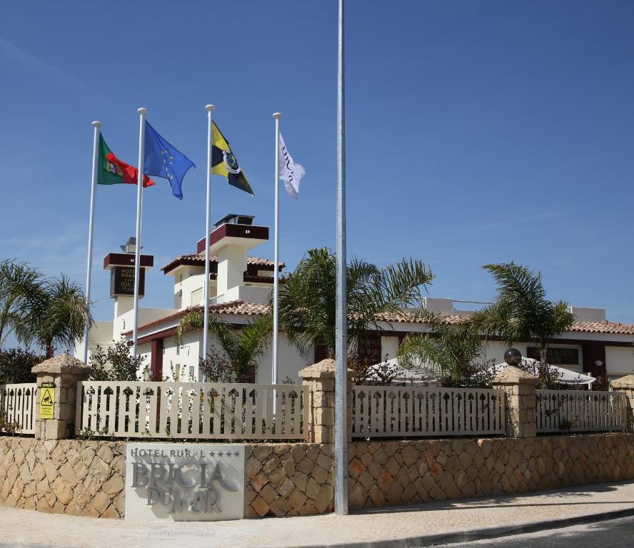 three flags flying in front of a building with a fence at Hotel Rural Brícia Du Mar in Ferragudo