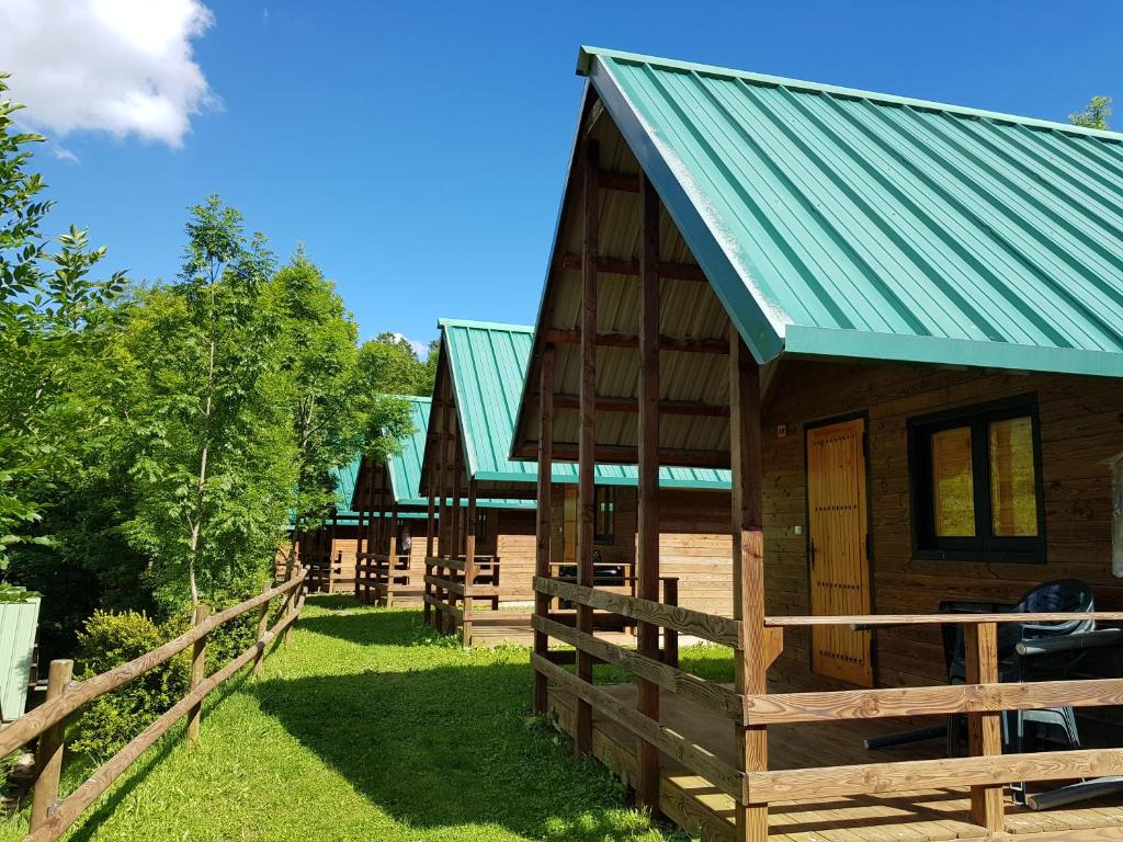 a wooden cabin with a green roof and a fence at Camping Vall de Ribes in Ribes de Freser