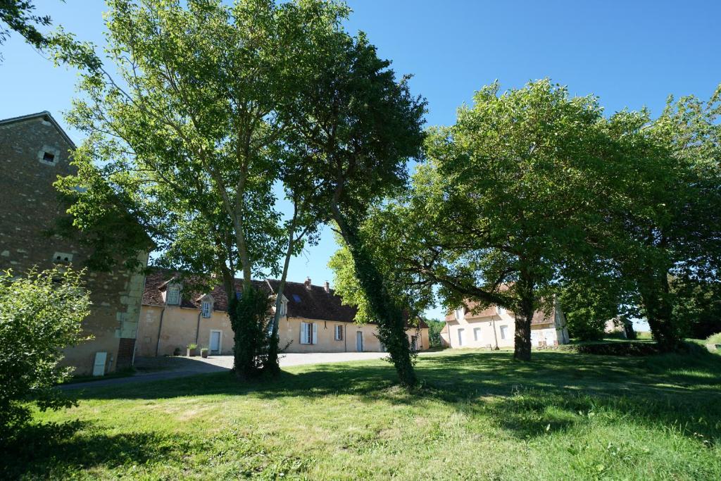 un groupe d'arbres dans une cour avec un bâtiment dans l'établissement Chambres d'hôtes du Bistrot des écuries, à Cour-Maugis-sur-Huisne