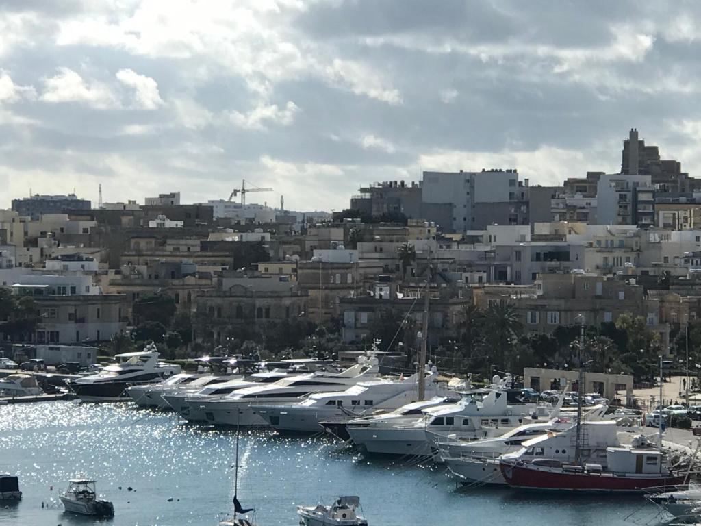 a bunch of boats docked in a harbor with a city at Sir William Strand in Il-Gżira