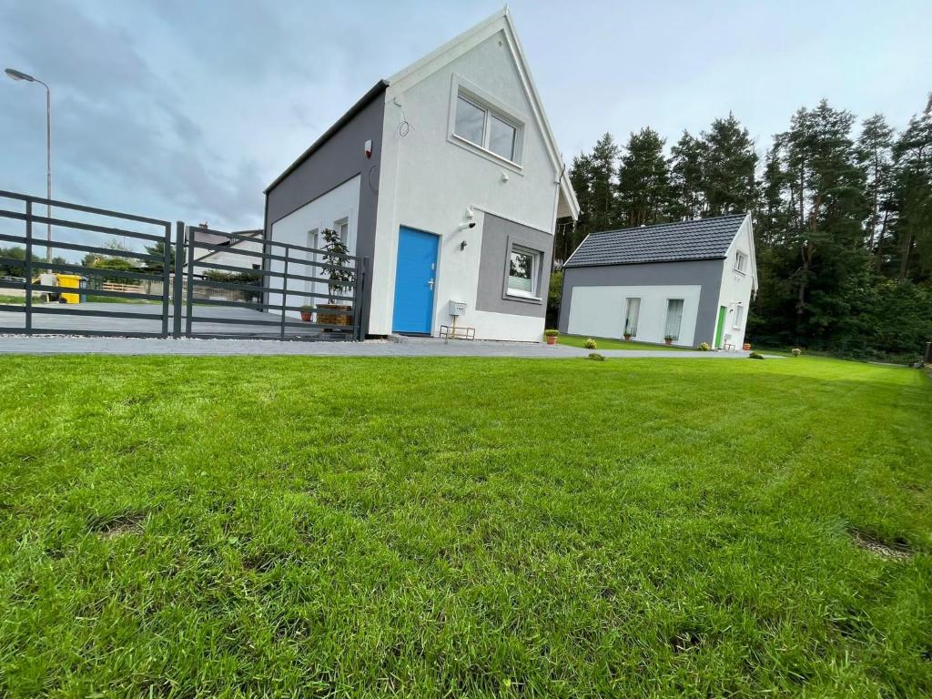 a white house with a blue door on a grass field at Ach Białogóra in Białogóra