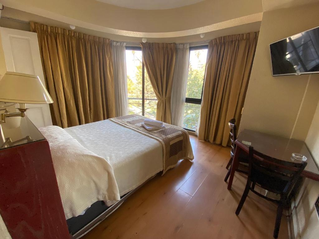 een slaapkamer met een bed, een bureau en ramen bij Intimo Hotel Miraflores in Santiago