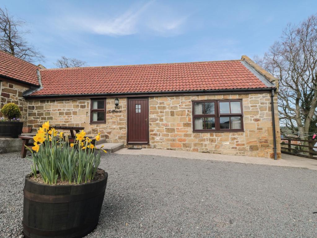 a small brick house with yellow flowers in front of it at The Calf House in Boosbeck