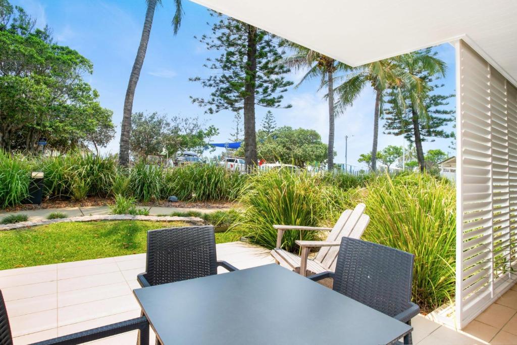 d'une terrasse avec une table, des chaises et des palmiers. dans l'établissement Unit 8 Plantation Resort Rainbow Beach, à Rainbow Beach