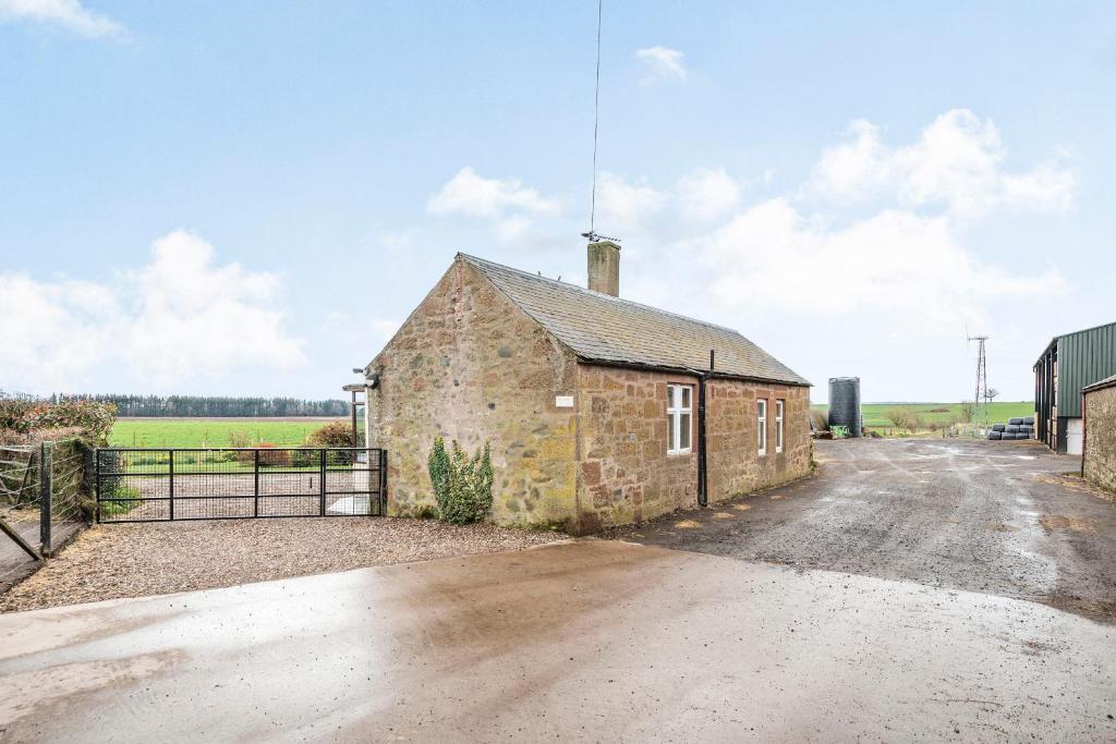 an old brick building with a fence next to a road at Steading Cottage in Kirriemuir