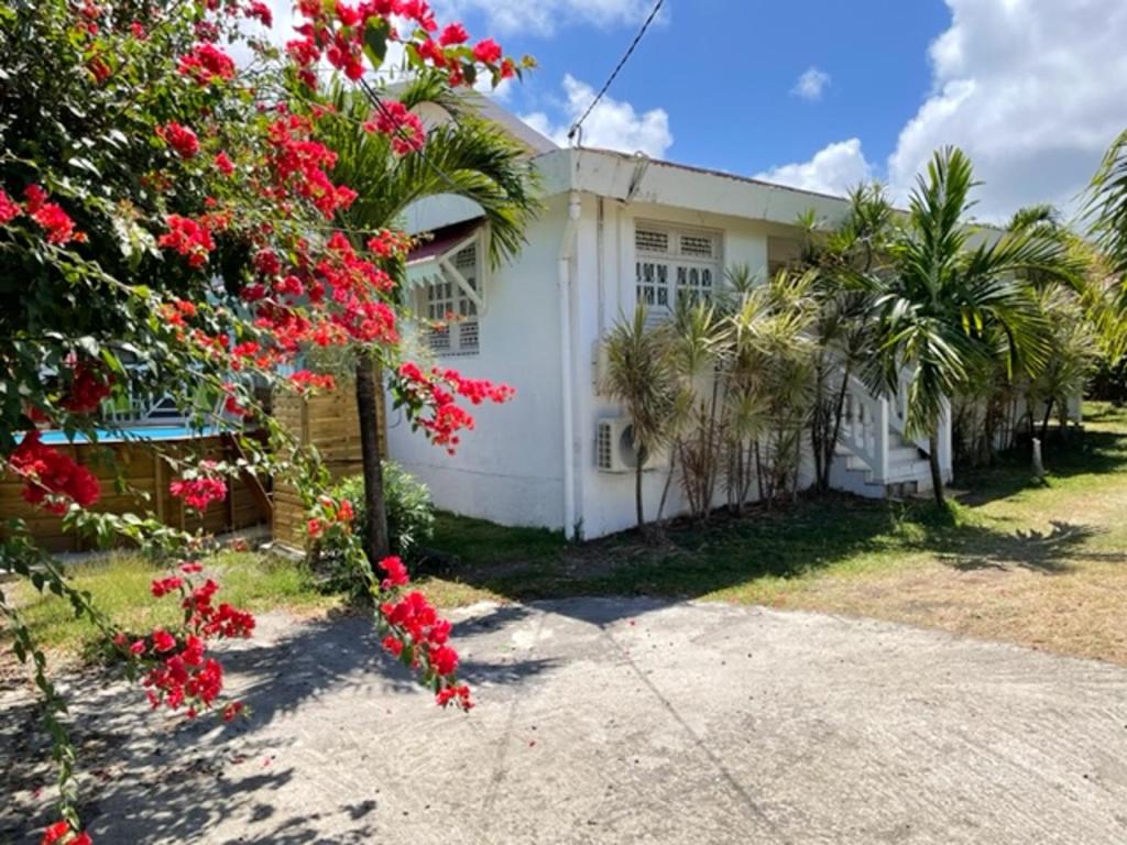 a white house with red flowers in front of it at Villa spacieuse avec piscine privée - Le Vauclin in Le Vauclin