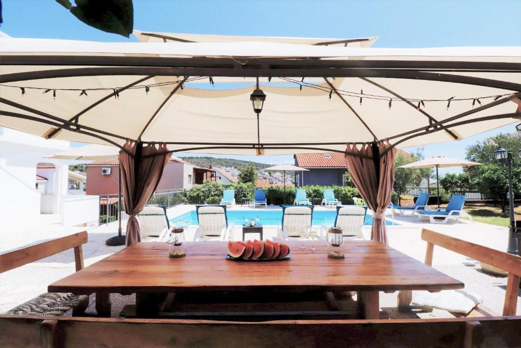 un tavolo di legno sotto un grande ombrellone accanto a una piscina di Villa Mendula Trogir - Luxury beachfront villa with large pool area surrounded by organic vegetable garden and olive trees a Trogir
