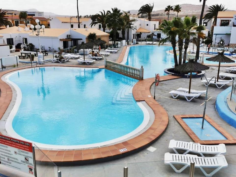 Una piscina en un resort con sillas y palmeras. en Puerta del Sol II (Caleta de Fuste), en Caleta de Fuste