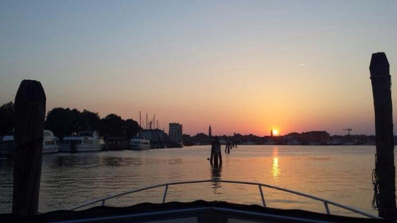 una barca in acqua con il tramonto sullo sfondo di Palazzo Giacchina a Sottomarina