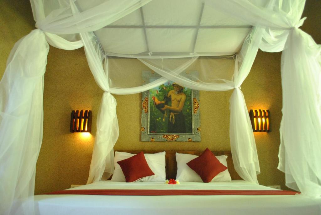 a bedroom with a canopy bed with red pillows at Pondok Rahayu Guest House in Pemuteran