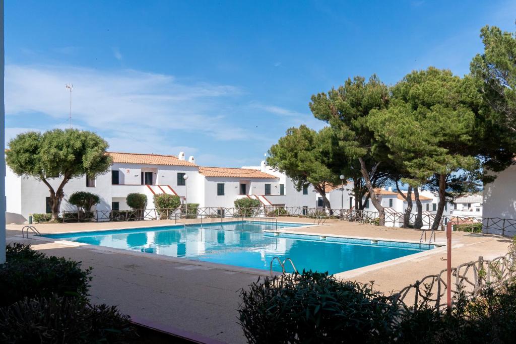 a swimming pool with trees in front of a building at Apartamento Menorca Arenal d'en Castell in Arenal d'en Castell