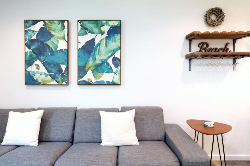 a living room with a gray couch and three paintings at Refreshing Renovation Walk to the beach in Kihei