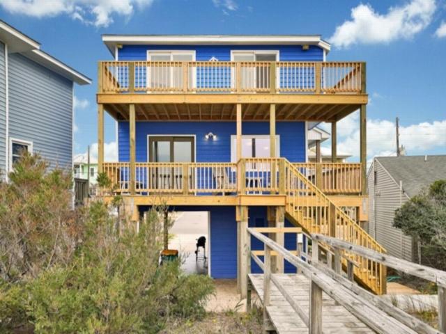 Una casa azul con terraza y un perro al frente. en Sea Haven - OCEANFRONT! Amazing master suite with a private oceanfront deck! Recently renovated and perfect for the entire family home, en Kure Beach