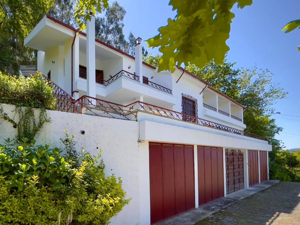 a white house with red garage doors at Villa Bouro - Breathtaking scenery near Gerês in Terras de Bouro