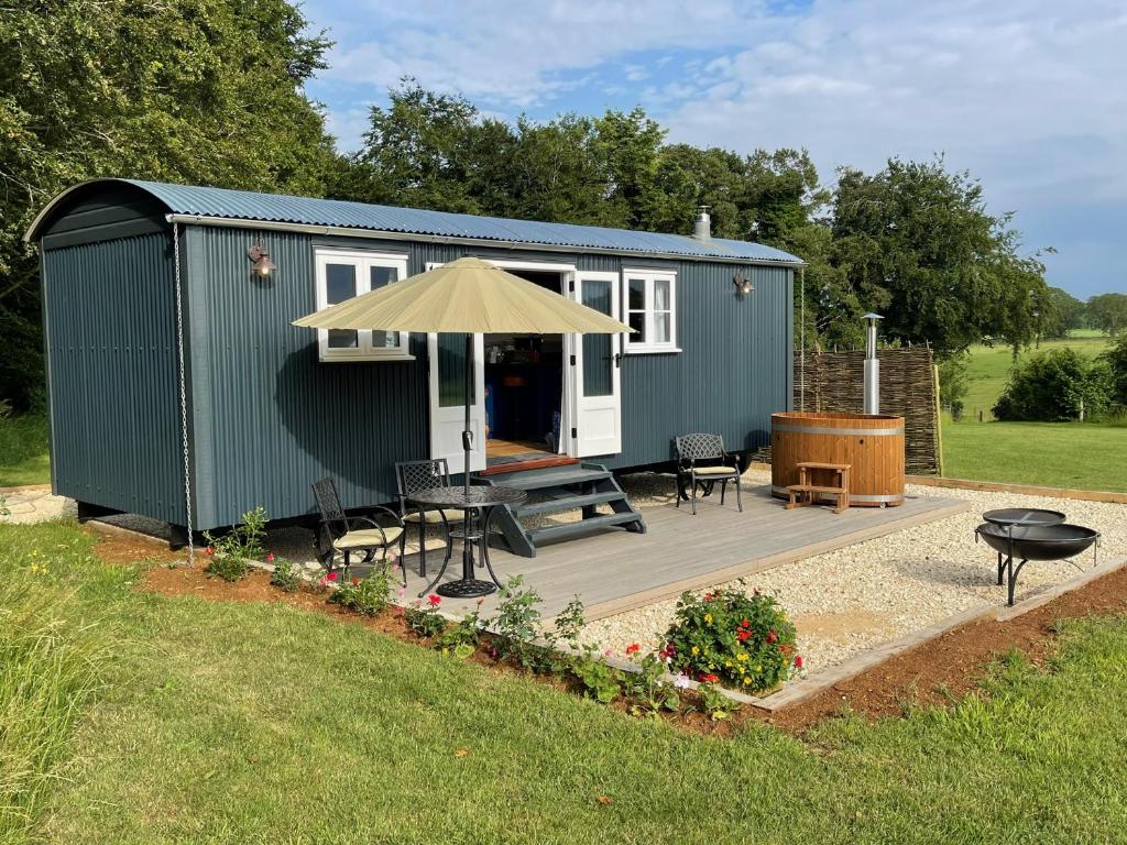 a green tiny house with a picnic table and an umbrella at 'The Barrington' - Westwell Downs Shepherd Huts in Burford