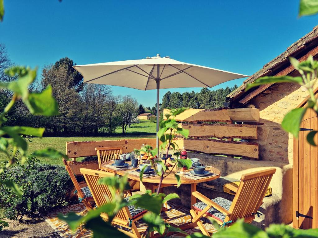 a table and chairs with an umbrella in a yard at La Ferme de Philomène - Gîte en Périgord Noir in Sainte-Foy-de-Belvès