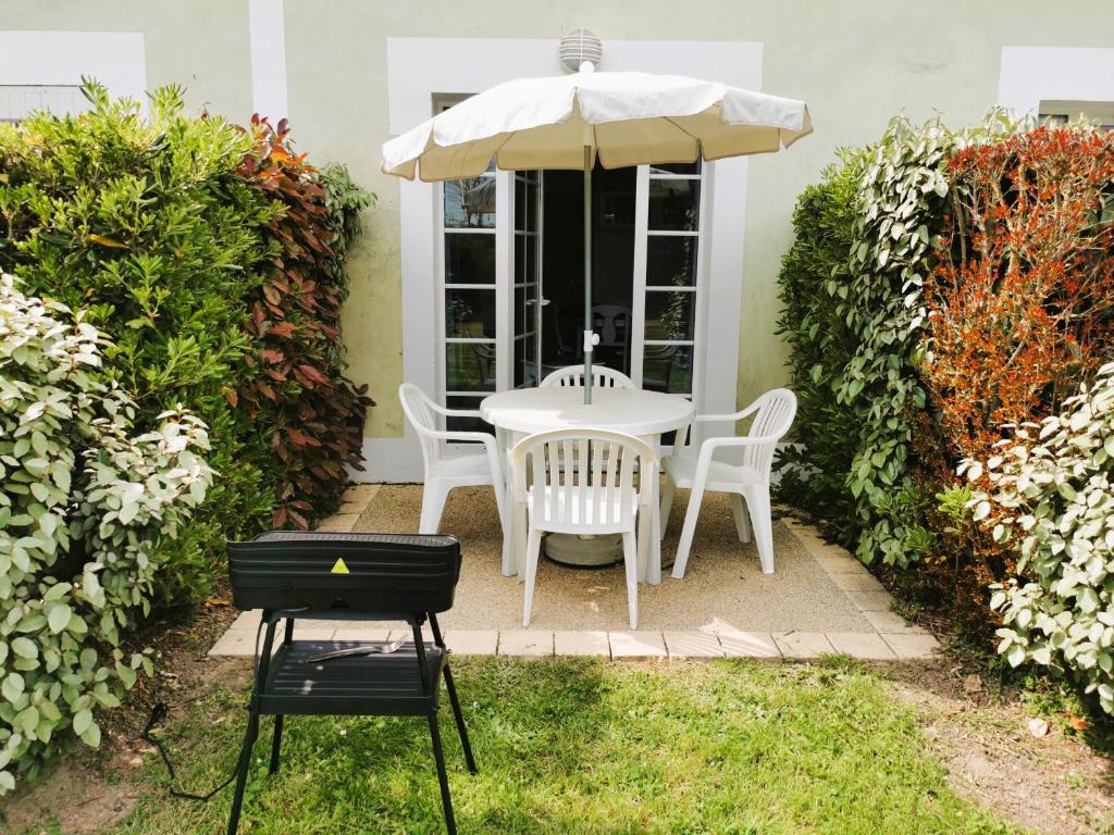 a white table and chairs under an umbrella at Le Bosquito - Piscine Avril a Septembre in Saint-Hilaire-de-Talmont