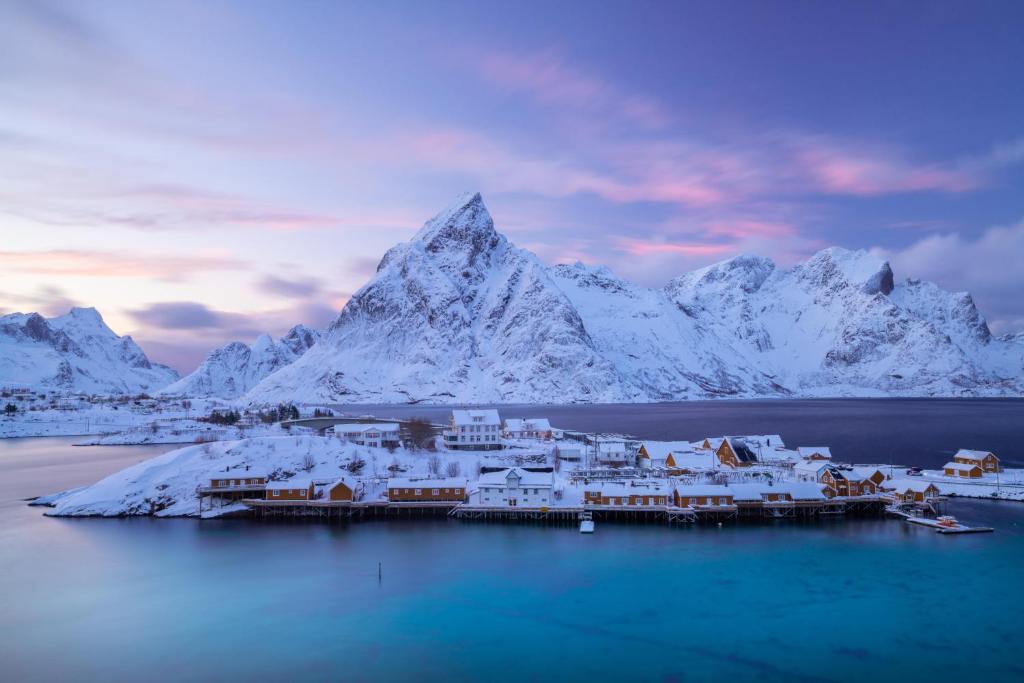 a town in the middle of the water with snow covered mountains at Sakrisøy Rorbuer in Reine