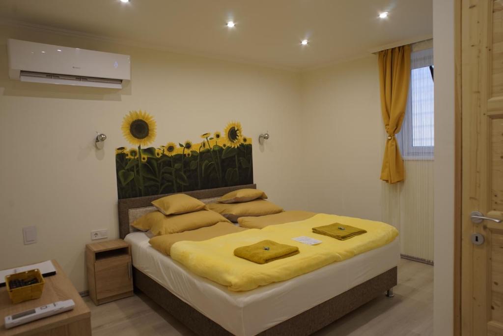 ein Schlafzimmer mit einem Bett mit gelben Laken und Blumen an der Wand in der Unterkunft Csengő Vendégház in Kiskőrös