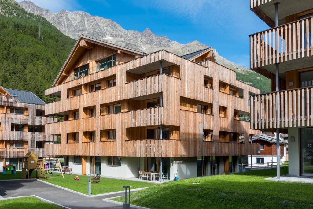 un bâtiment en bois avec des montagnes en arrière-plan dans l'établissement Montela Apartments by fewo-plan SAAS215, à Saas-Grund