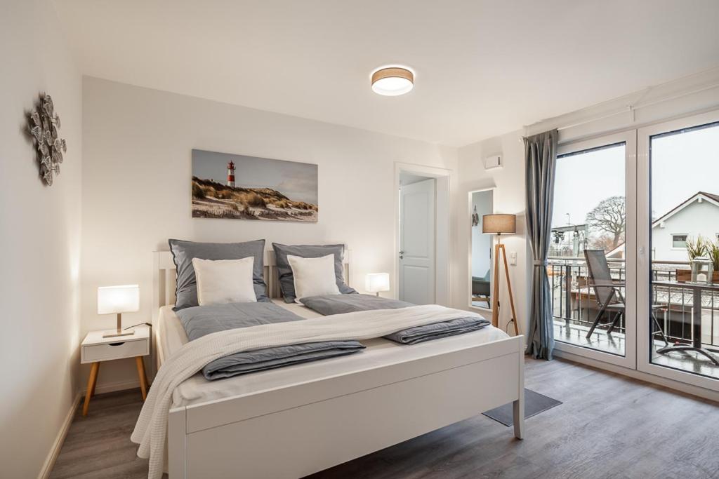 a white bedroom with a large bed and a balcony at Apartment Seagull in Neustadt in Holstein