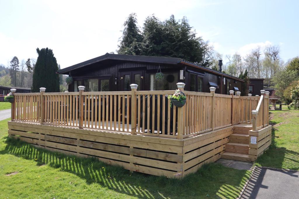 a house with a wooden fence in the grass at HEDDFAN, Luxury 3 bedroom timber lodge, Caer Beris Holiday Park, Builth Wells in Builth Wells