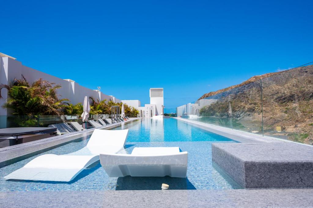 una piscina con 2 sillas blancas y una piscina en New Luxury Apartment First Line Sea View en El Palmar