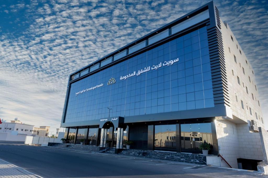 a large glass building with a sign on it at Sweet Light Serviced Apartments in Tabuk