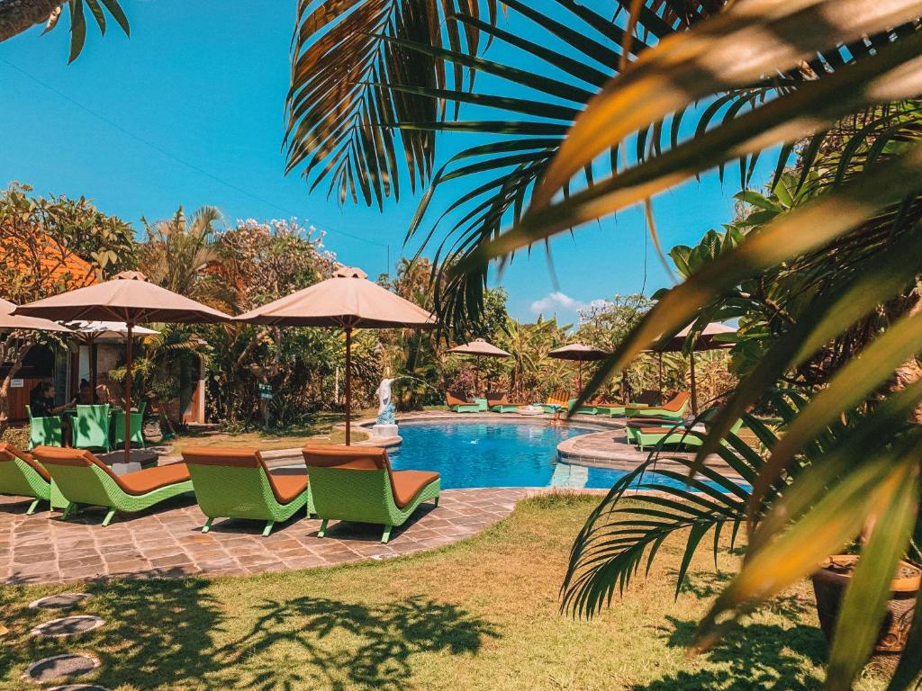 una piscina con sillas y sombrillas verdes en Bali Wirasana Inn en Sanur