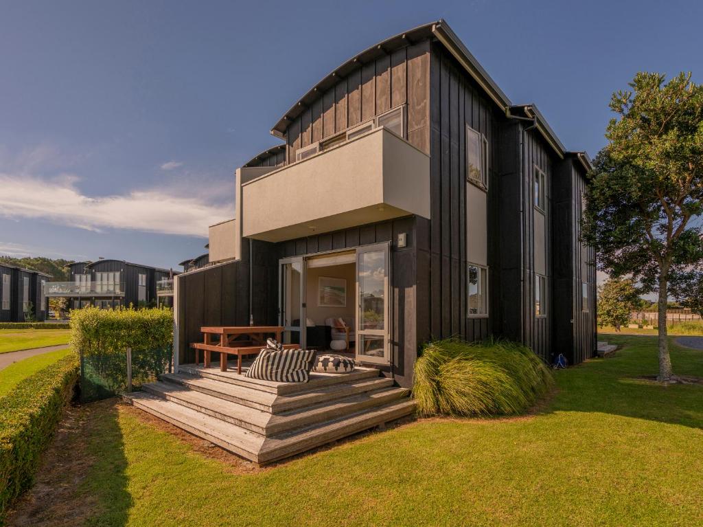 Casa negra con porche de madera y banco en Sunset Retreat - Matarangi Holiday Home, en Matarangi