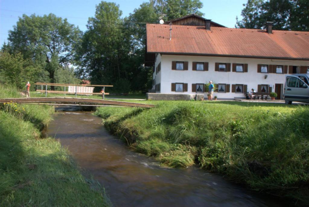 uma ponte sobre um rio em frente a um edifício em Ferienhaus, Bauernhof mit Angel- und Badesee, Roßhaupten, Allgäu em Roßhaupten