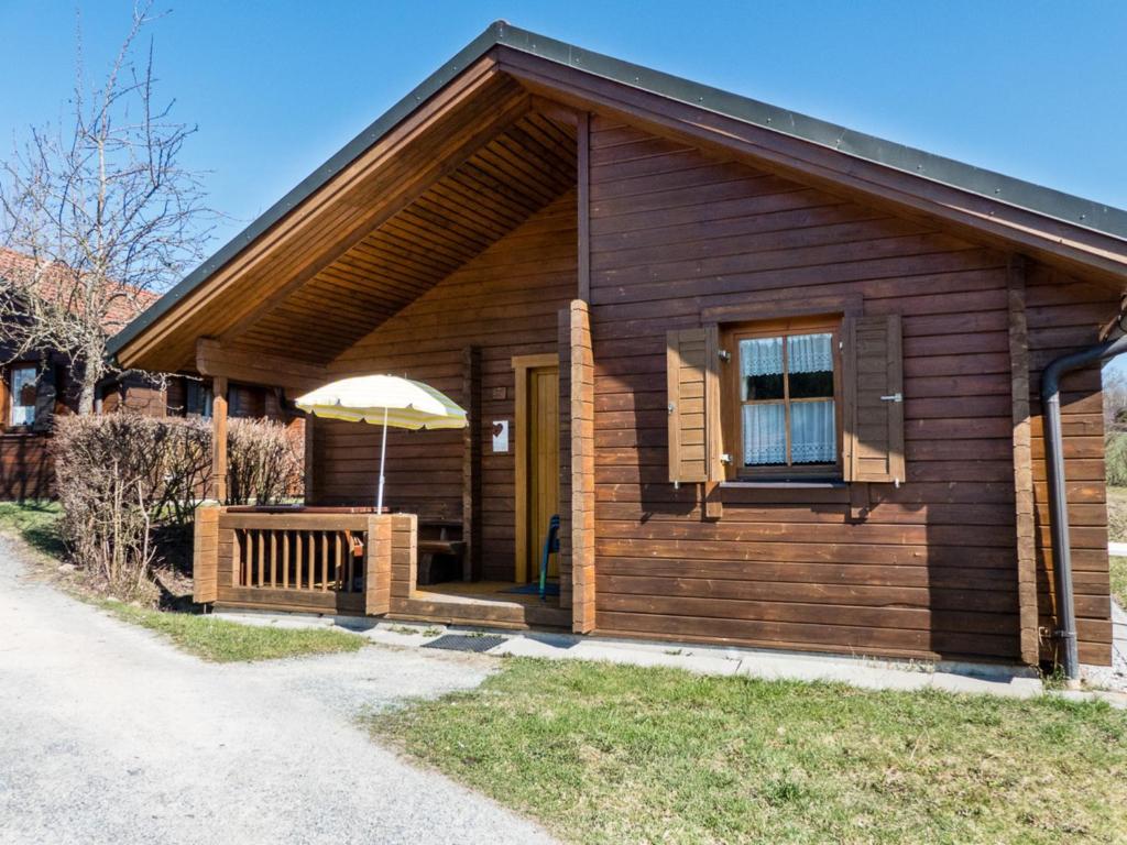 eine Holzhütte mit einem Sonnenschirm und einer Veranda in der Unterkunft Ferienhaus Nr 14, Typ A, Feriendorf Jägerpark, Bayerischer Wald in Viechtach