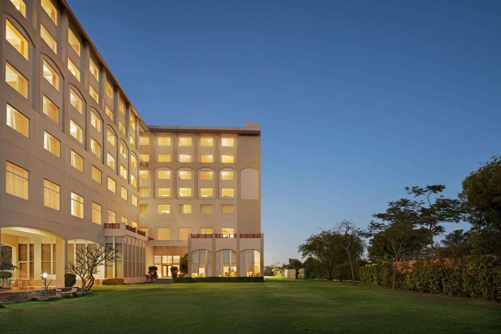 a large building with a lawn in front of it at Ramada by Wyndham Jaipur Jaisinghpura in Jaipur
