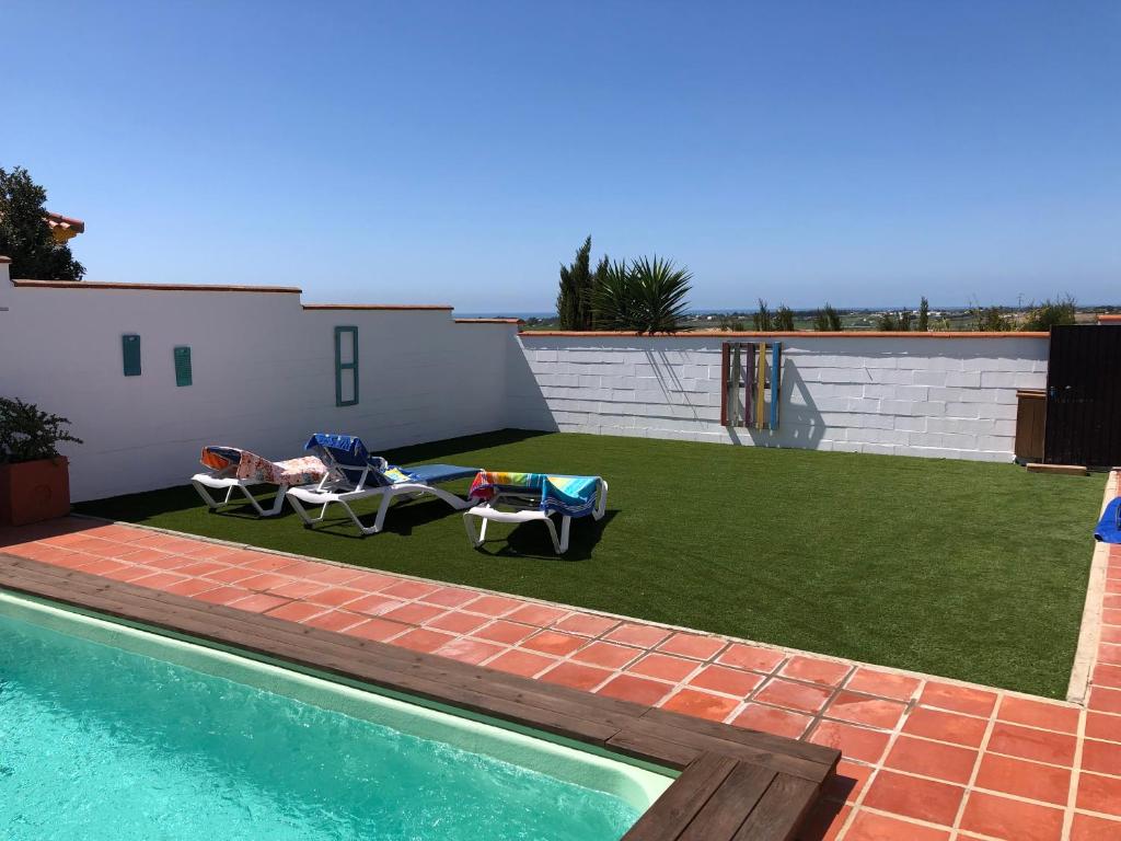 un patio trasero con piscina y césped con 2 sillas en El Mirador de Bellavista, en Conil de la Frontera